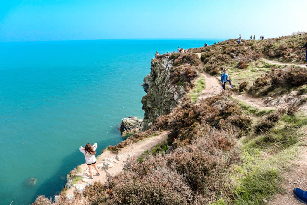 The vibrant Howth Cliff Walk in Ireland, with people hiking along the rugged coastal path above the blue sea