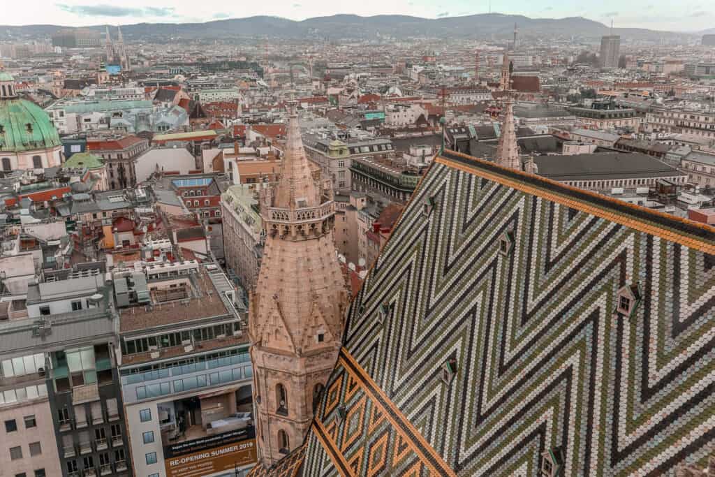 Aerial view of Vienna's St Stephen’s Cathedral's colorful tiled roof with the city's historic and modern buildings in the distance