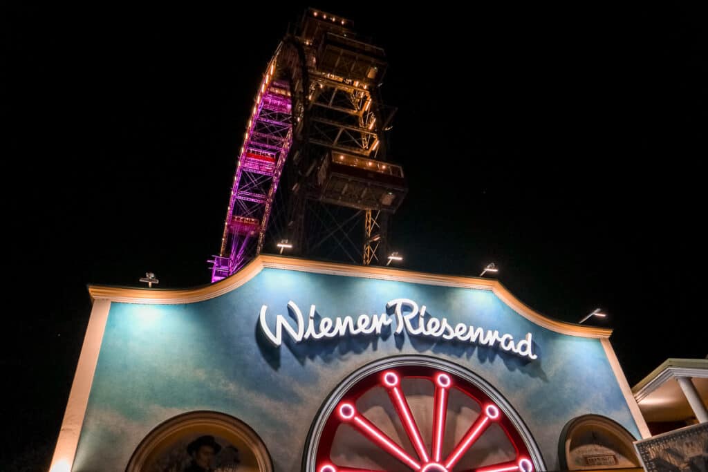 Night view of the iconic Wiener Riesenrad Ferris wheel in Vienna, illuminated in purple with the entrance's vibrant signage