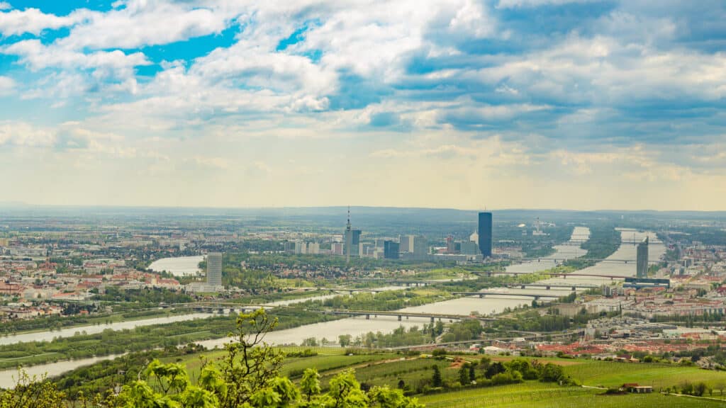 A panoramic view of Vienna from the Kahlenberg hill, showcasing the winding Danube River and cityscape against a backdrop of dramatic clouds