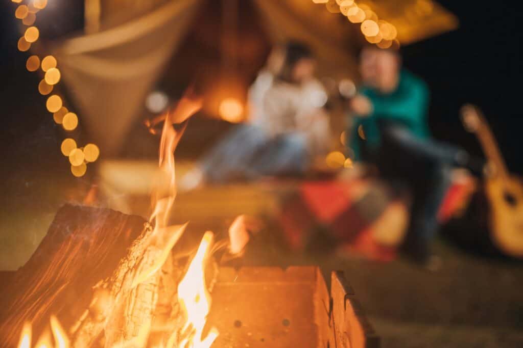 Blurred foreground of a campfire with a couple enjoying a cozy evening in a tent, illuminated by warm string lights