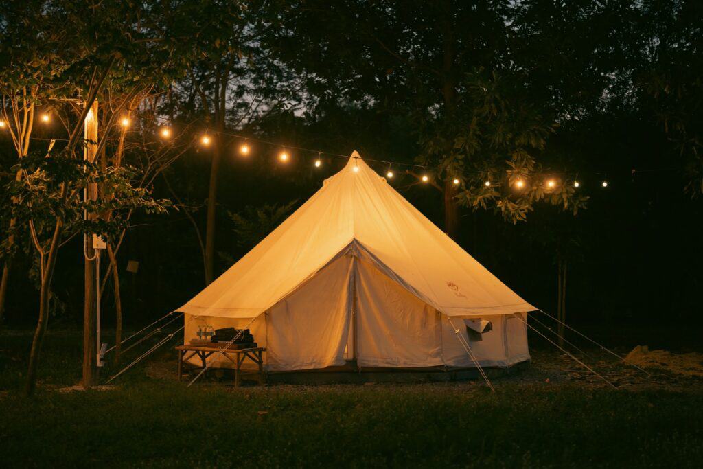 A bell tent illuminated by warm string lights at night, creating a cozy camping atmosphere in a forest clearing