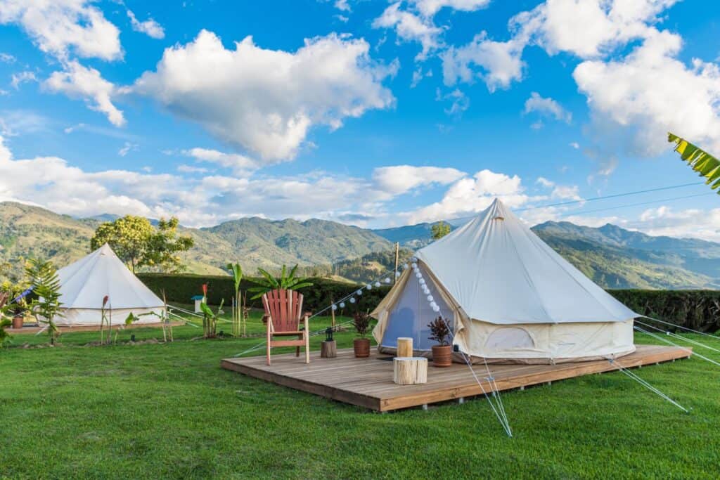  tranquil glamping scene with a bell tent set up on a lawn against a backdrop of mountainous landscape and a cloudy sky