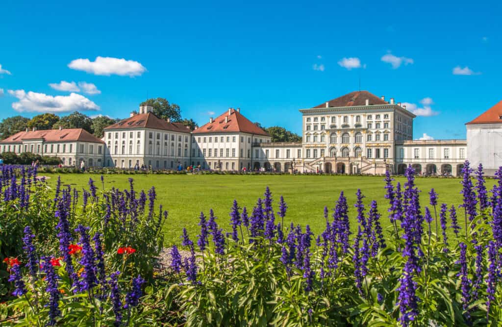 The elegant Nymphenburg Palace in Munich surrounded by lush gardens with purple salvia flowers in full bloom