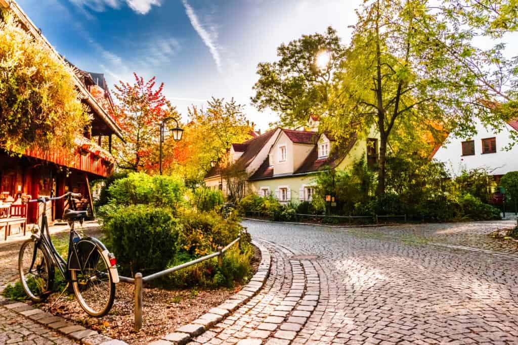 A peaceful cobblestone street in a quaint Munich neighborhood with traditional houses and lush autumn foliage
