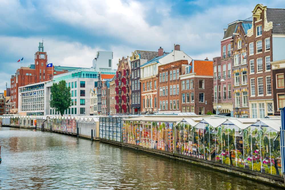 The colorful and bustling Bloemenmarkt, Amsterdam's floating flower market, with a variety of flowers displayed in glasshouse stalls.
